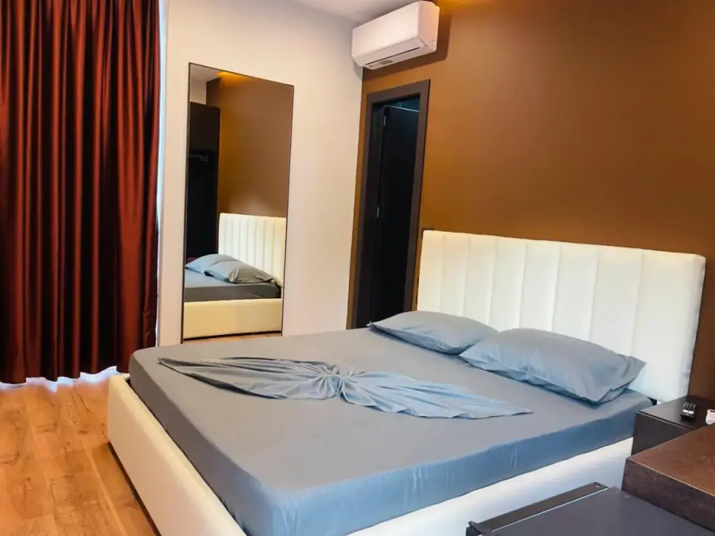 The same room from the window side, the white padded headboard against a brown wall beside a full-length mirror