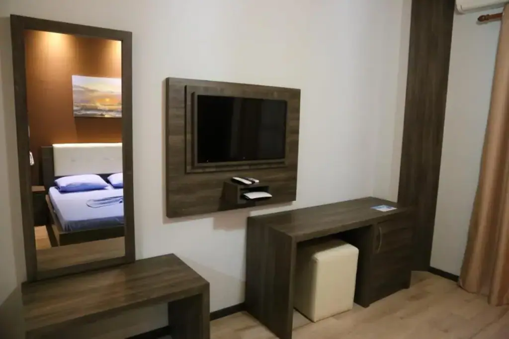 A room with a desk, a wall mirror and a television on a wood panel beside the balcony door