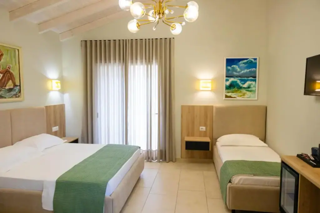 A room with two beds under a boarded ceiling, a brass chandelier and framed paintings on the walls