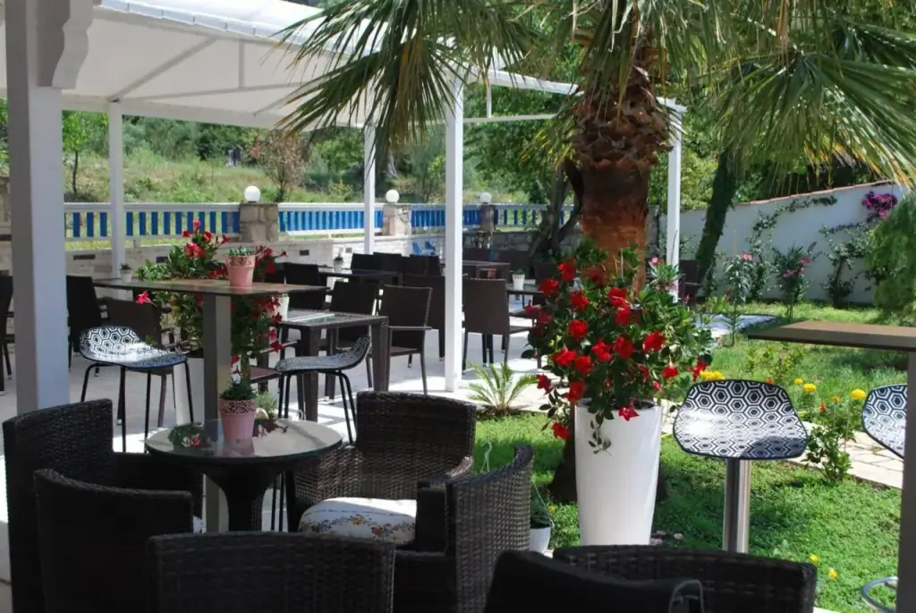 Wicker tables and chairs under a white canopy beside a palm and pots of red geraniums