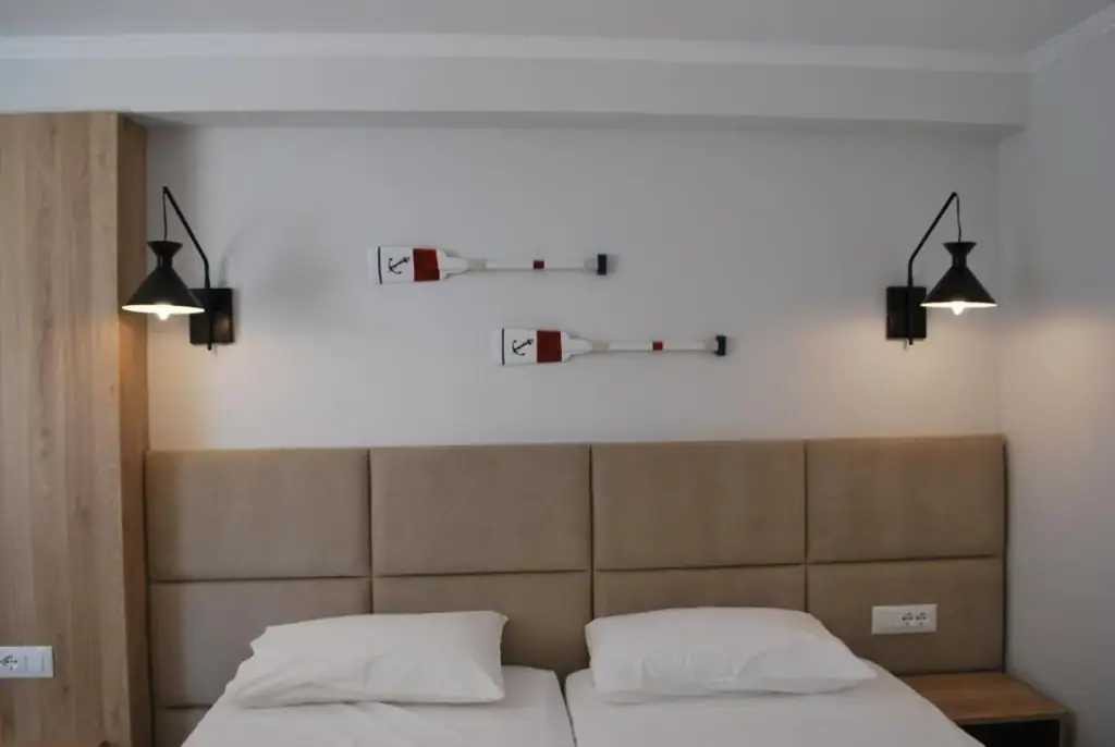 An upholstered headboard between two black wall lamps, with a framed painting beside it