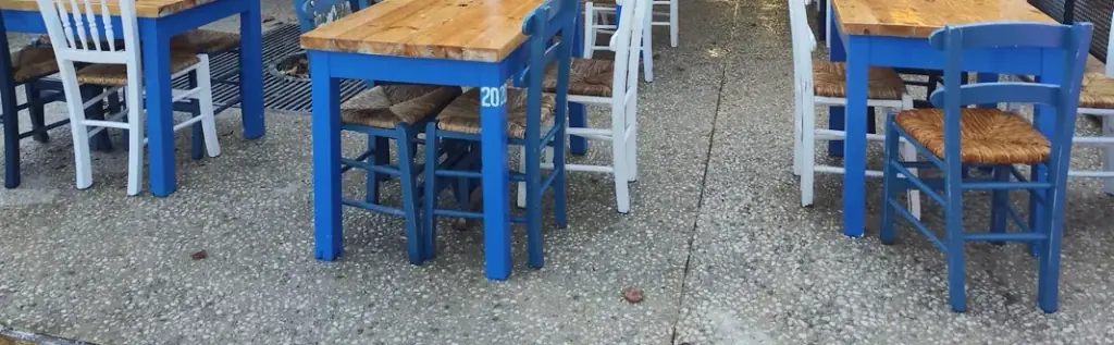 Cobalt-blue tables with bare wood tops, and white and blue rush-seat chairs, on the pebble-wash concrete of the terrace