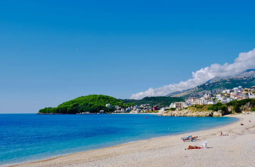 A long sweep of Albanian Riviera beach backed by mountains and a hillside village