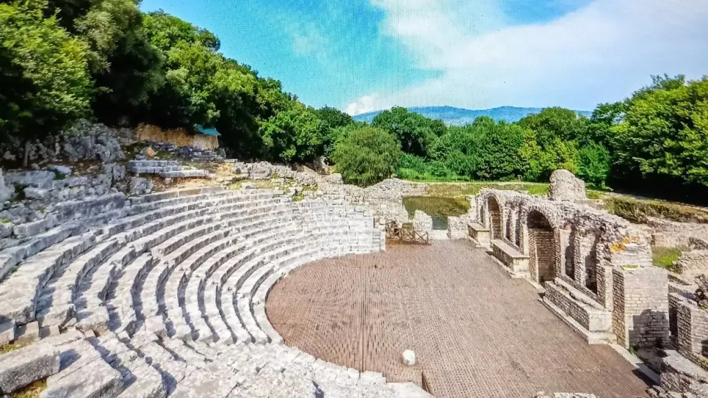 The ancient Greek theatre at Butrint, curved stone seating rows surrounded by forest under bright light