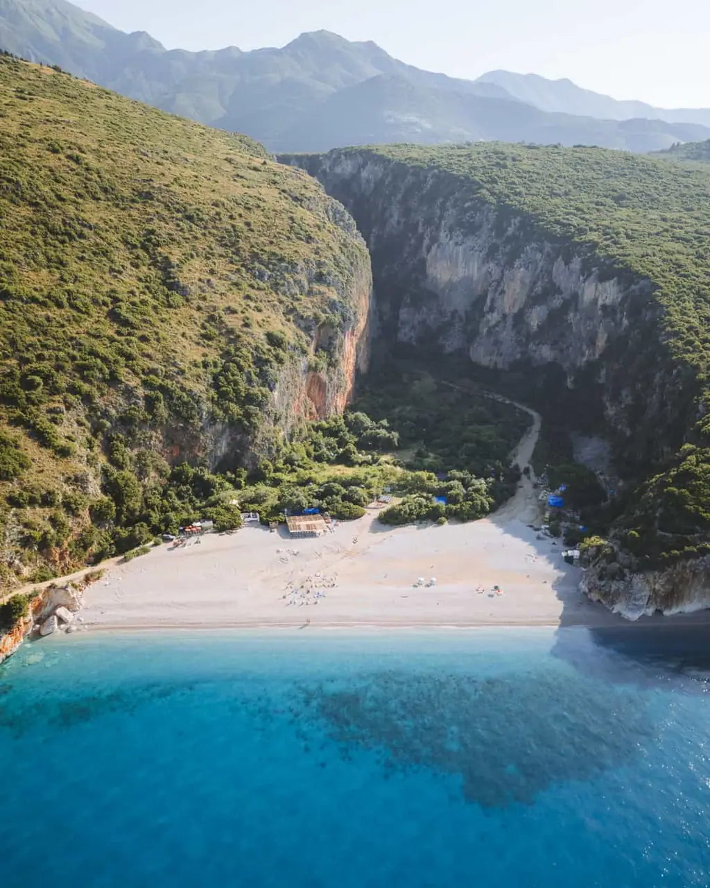 Trail descending through Gjipe Canyon to the turquoise beach below, May 2026