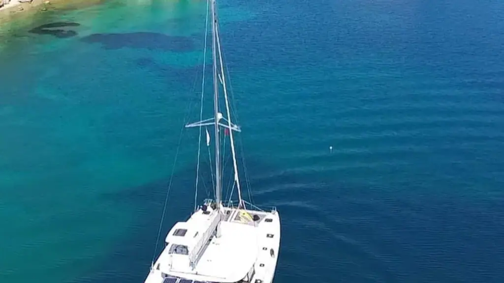 A white catamaran anchored on flat deep-blue water off the Ksamil coast under a clear sky