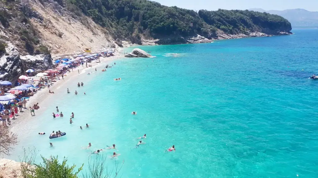 Ksamil's turquoise bay and small offshore islets seen in bright midsummer light, sunbed rows filling the white sand