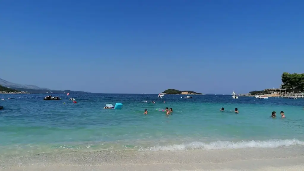 Clear turquoise water and pale sand at Ksamil with small wooded islets offshore under soft light and almost no people