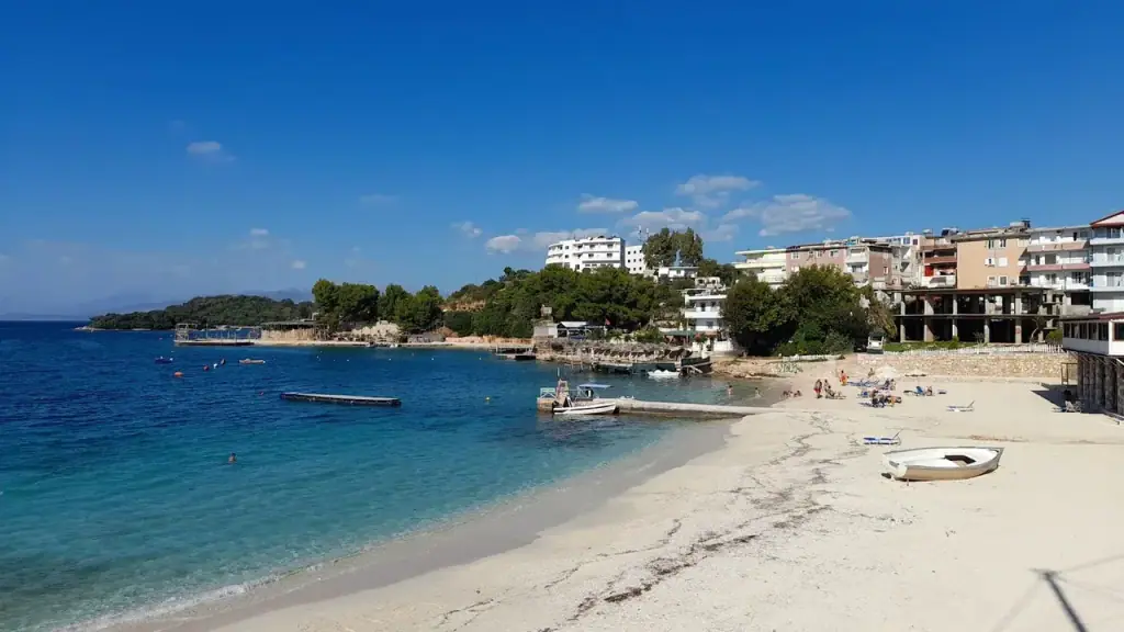 Ksamil's beachfront with buildings and parked cars along the road edge above the sand and turquoise bay