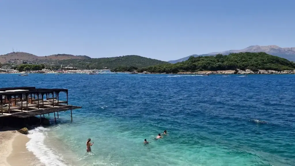 A low concrete jetty running into shallow clear water at Ksamil with swimmers in the calm turquoise shallows