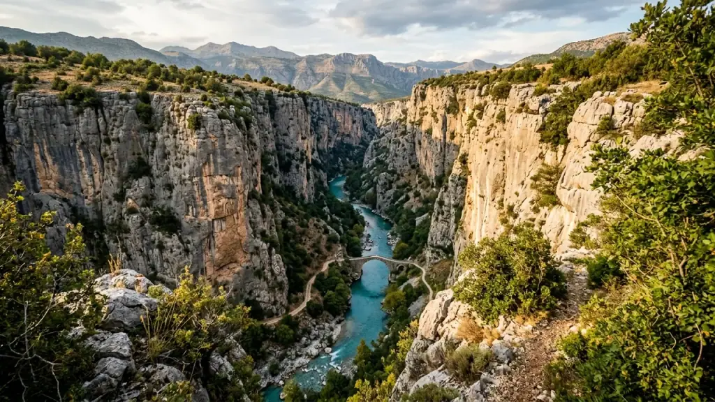 A deep limestone gorge with vertical rock walls dropping to a turquoise river in southern Albania