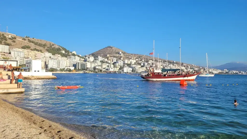 Saranda bay in the evening with moored boats on calm water and the lit town curving around the shoreline