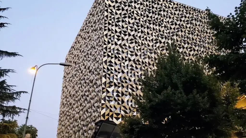A distinctive patterned tower rising above trees on a Tirana street under a pale sky