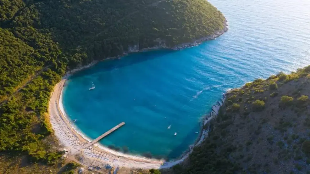 Kakome Bay from the air, a horseshoe of turquoise water with a jetty and rows of sunbeds on the shingle
