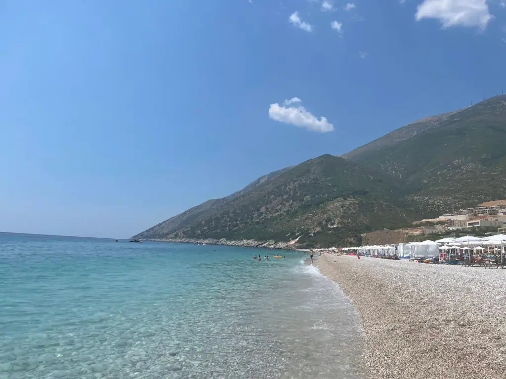 The long pale-pebble shore and clear turquoise water of Palasë Beach below the Llogara mountains on the northern Albanian Riviera