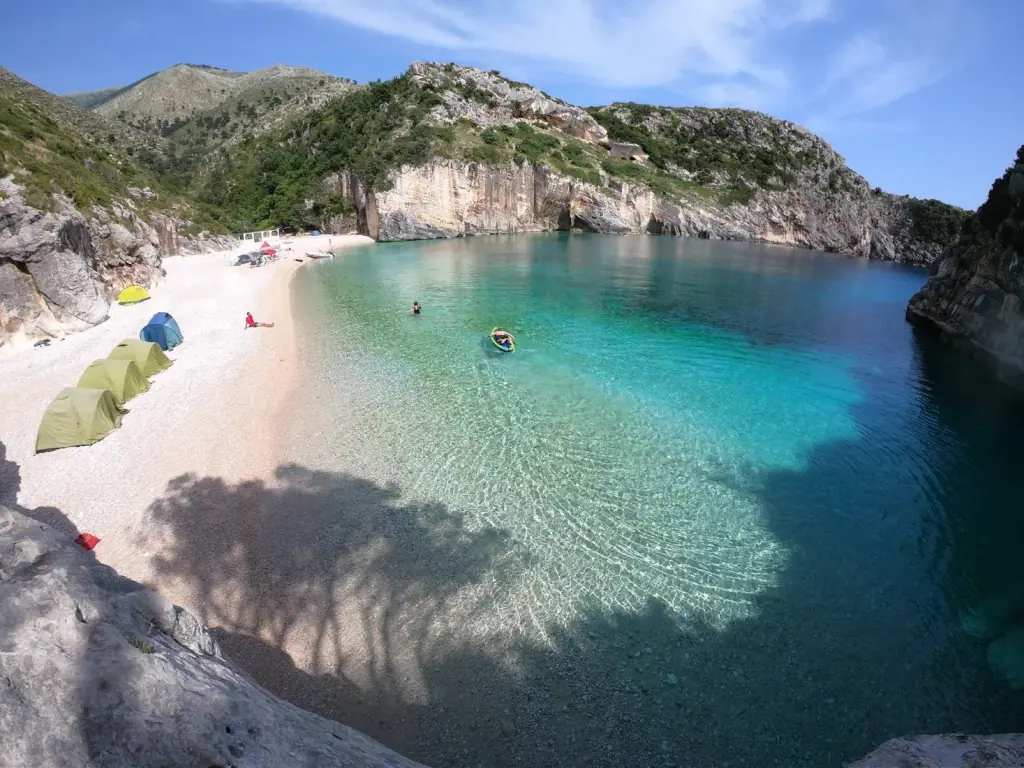 Pebble cove at Grama Bay with tents on the shore and a kayak in turquoise shallows