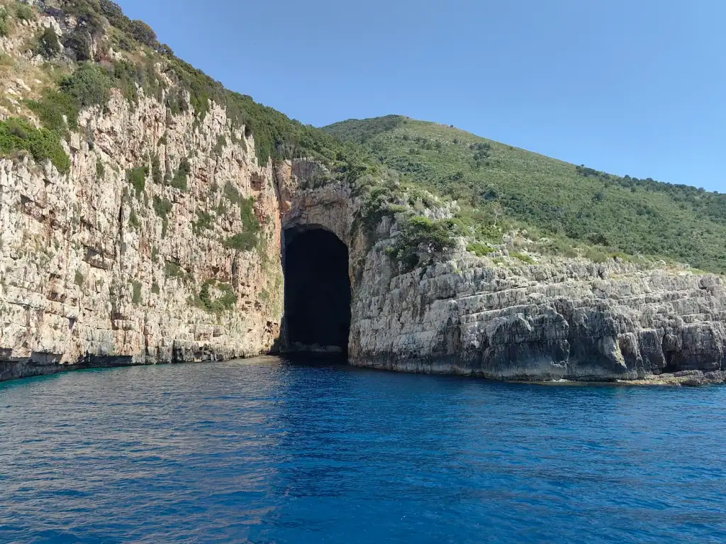 Large dark sea-cave entrance in white limestone cliffs over deep blue water on the western Karaburun peninsula