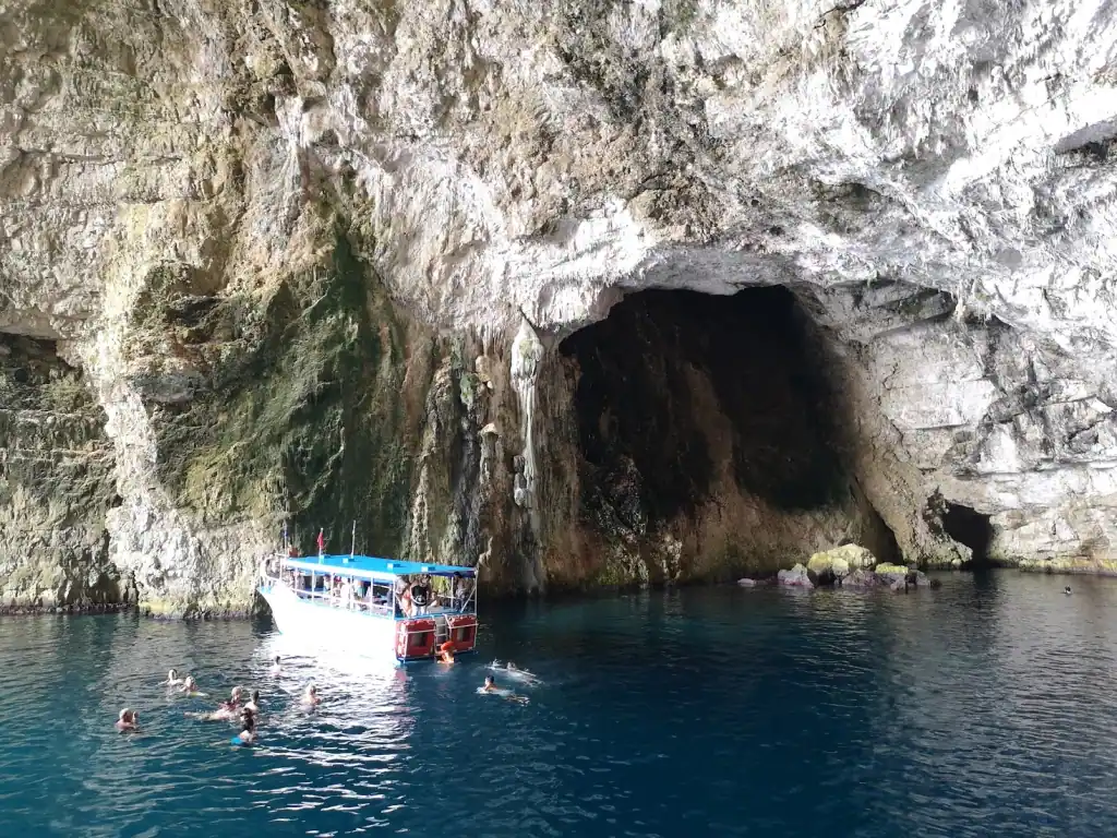 A tour boat and swimmers outside the mouth of Haxhi Ali Cave