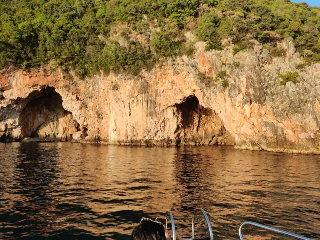 Cave mouth in the orange rock face above still water