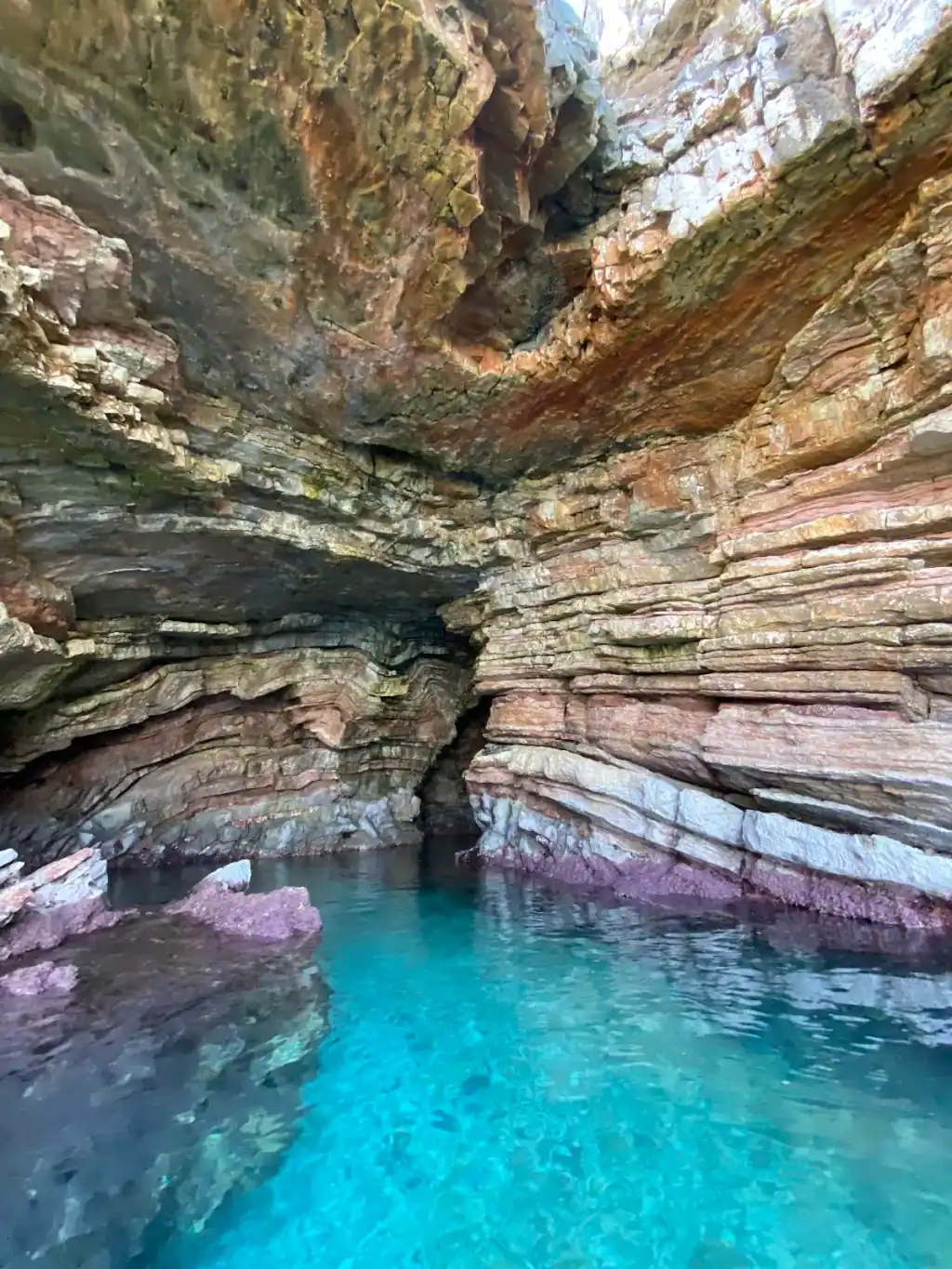 Inside Turtle's Cave near Saranda, layered pink and grey rock arching over bright turquoise water