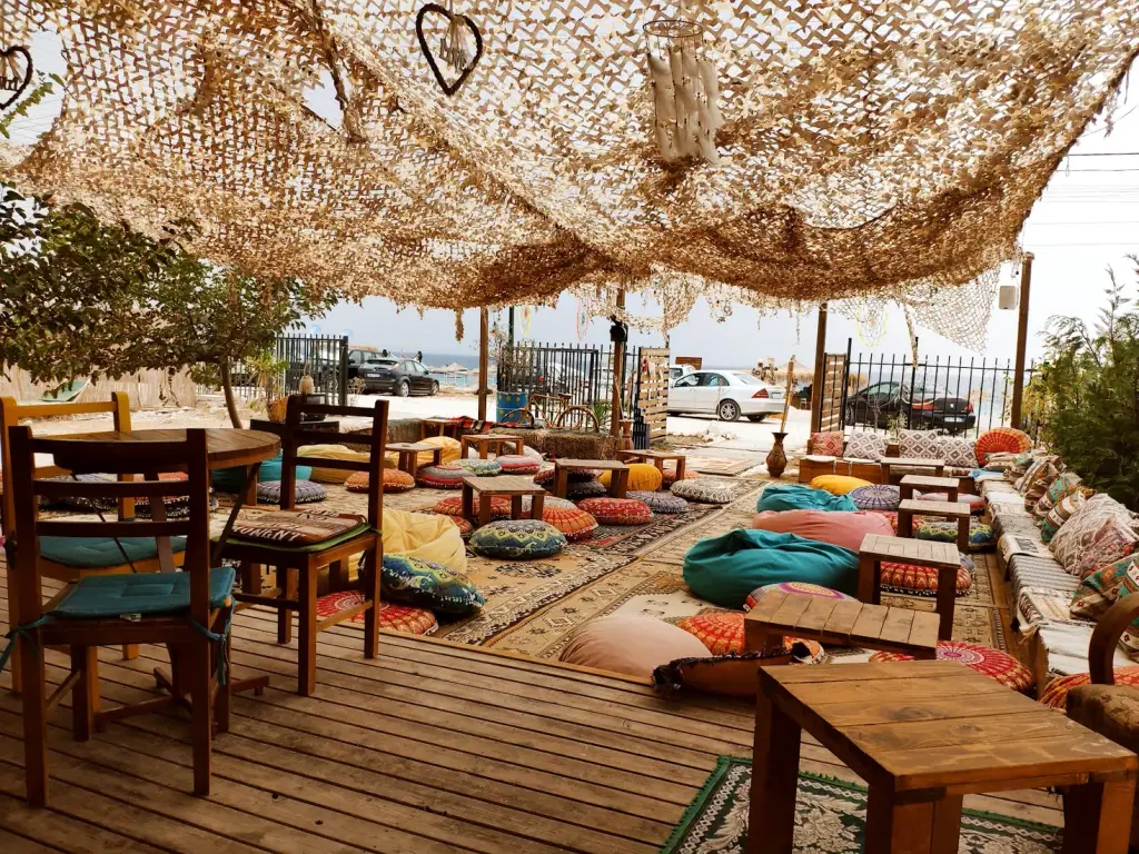 BOHO Livadh beach bar's lounge area with floor cushions, rugs and a fishing-net canopy by the sea