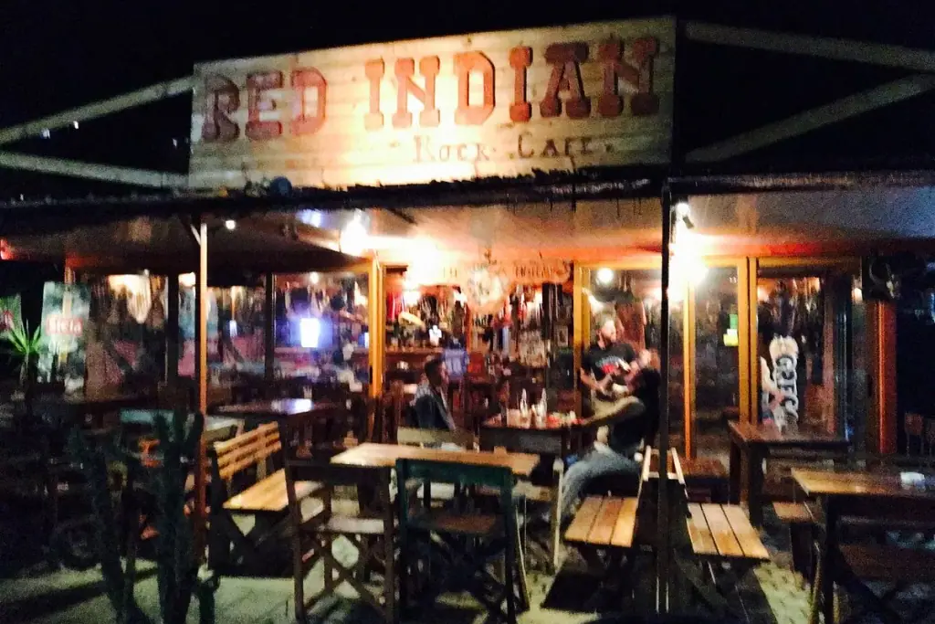 Rock-themed facade of Red Indian Rock Cafe with its painted sign and red chairs beside the highway