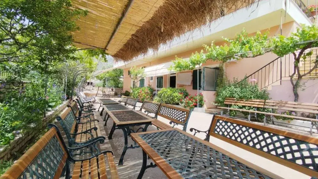 Shaded garden terrace with benches and communal tables at Oasis Hostel in Himara