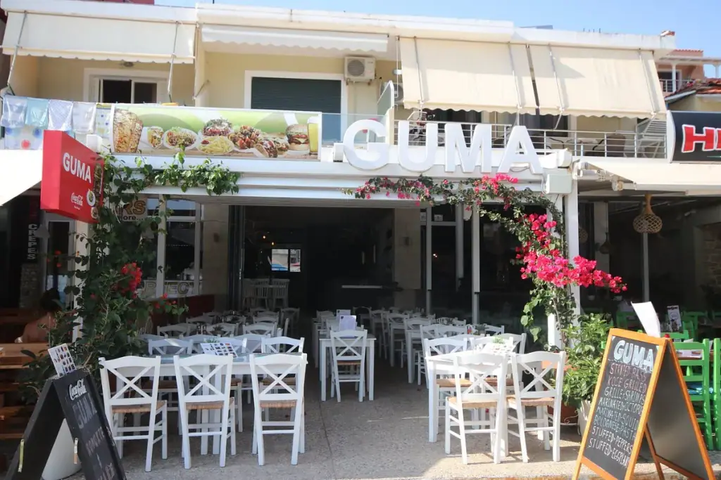 Street-front storefront with the GUMA sign and white outdoor chairs at Guma Restorant in Himara