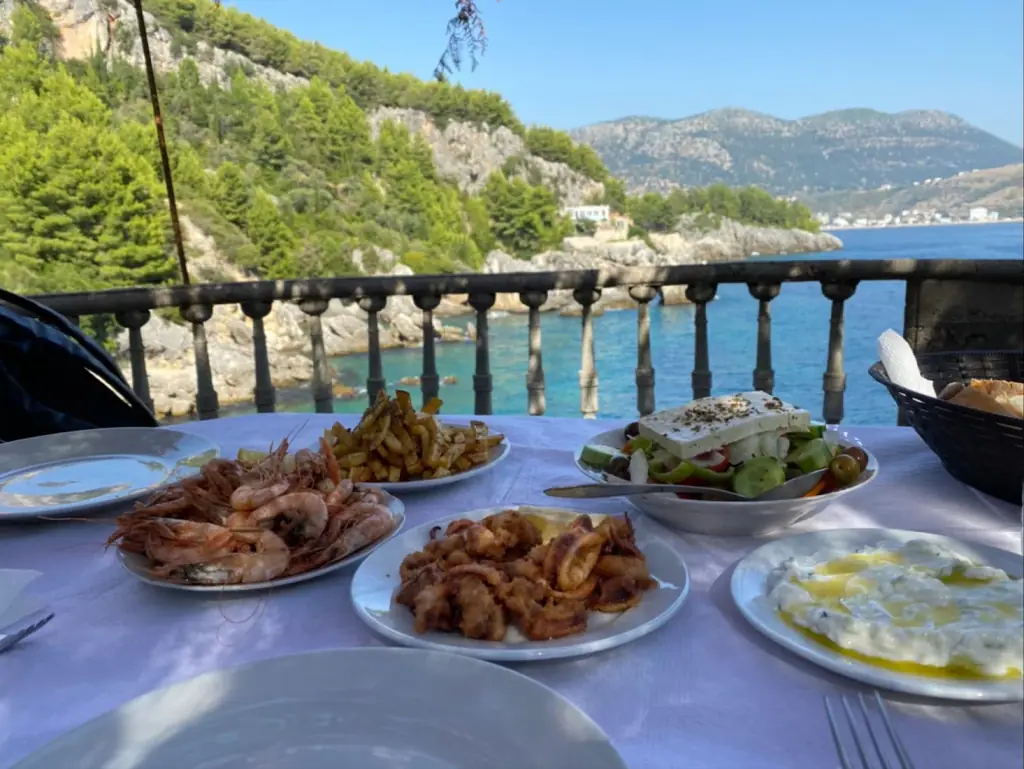 A terrace table of shrimp, fried calamari, Greek salad and tzatziki above a turquoise rocky cove at Kilimani Retreat in Himara