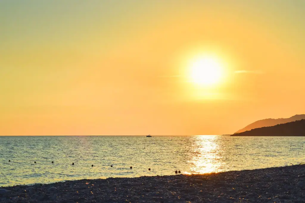 Sunset over Livadhi Beach, the sun low on the water above the pebble shore