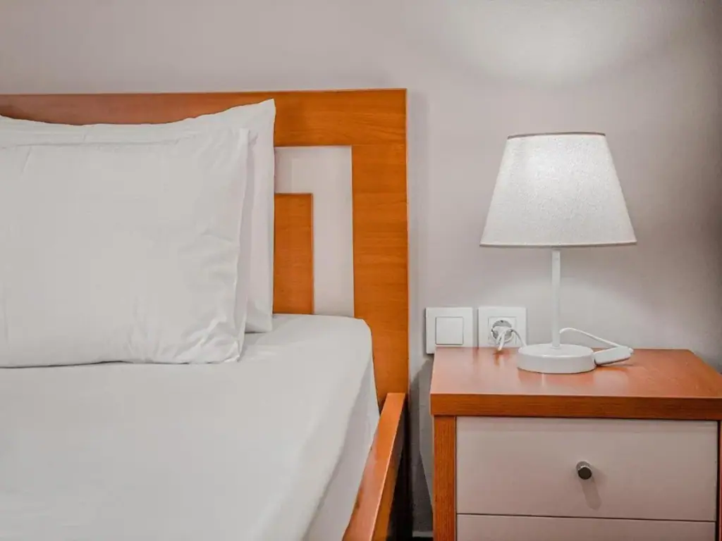 A bedside table, lamp and power sockets beside a wooden headboard at Kleanthi's Hotel