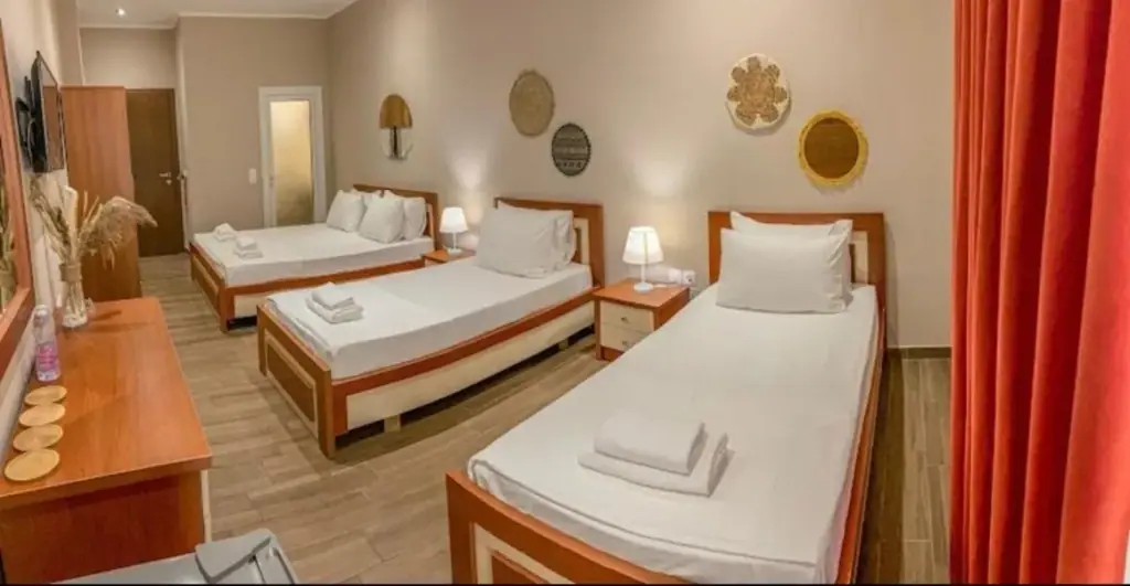 A room at Kleanthi's Hotel with three beds, bedside lamps and a red curtain at the balcony door