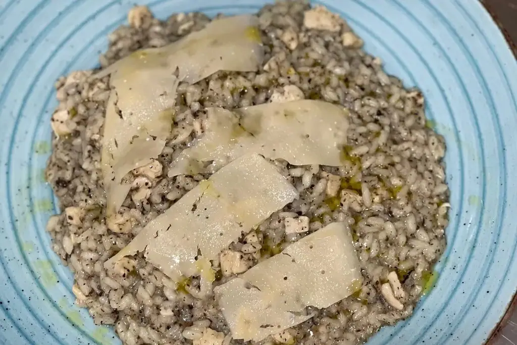 A rice dish finished with shaved hard cheese and olive oil, on the kitchen's pale blue plate.