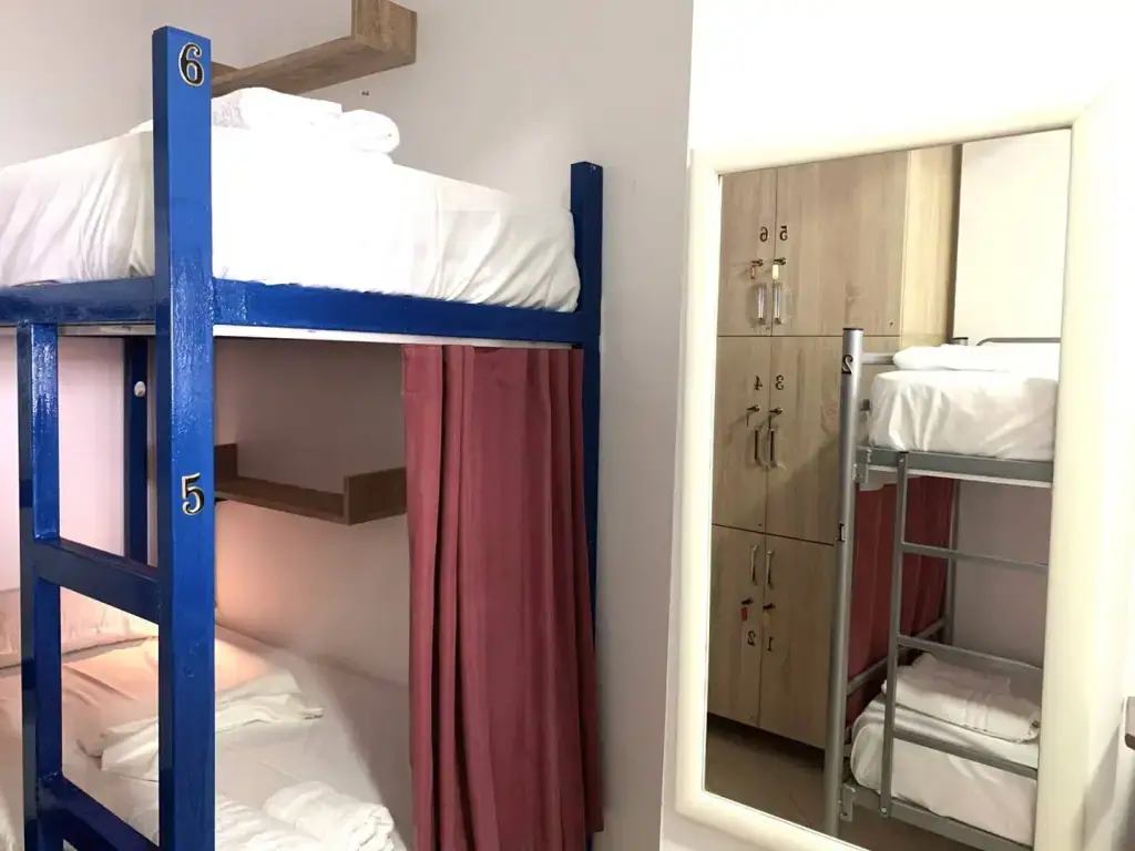 A blue-painted bunk bed with the numbers 5 and 6 on its frame, a dark red curtain drawn back, and a mirror reflecting numbered lockers