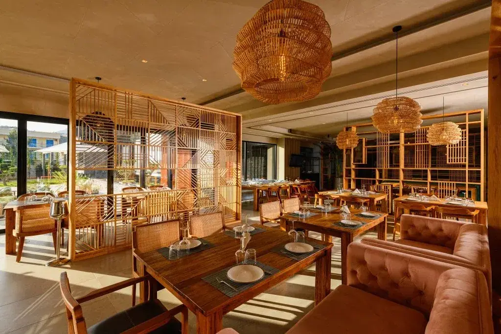 The Miamar dining room — timber lattice screens, rattan pendant lamps, teak tables and a dusty-rose velvet banquette