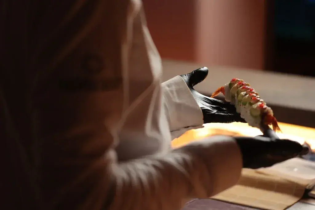 A chef finishing a sushi roll over the warm-lit counter of the Miamar sushi lounge