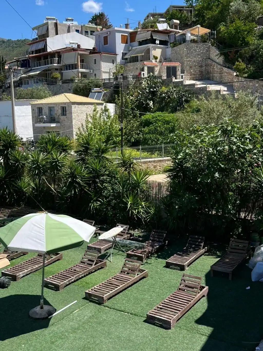 Rows of pallet sun loungers on green turf below the stone houses of Potam