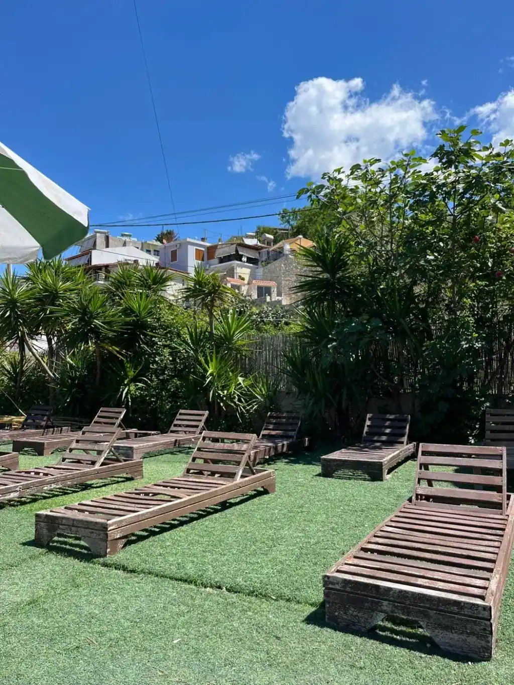 Wooden sun loungers on artificial turf under a green and white parasol with the village on the slope behind