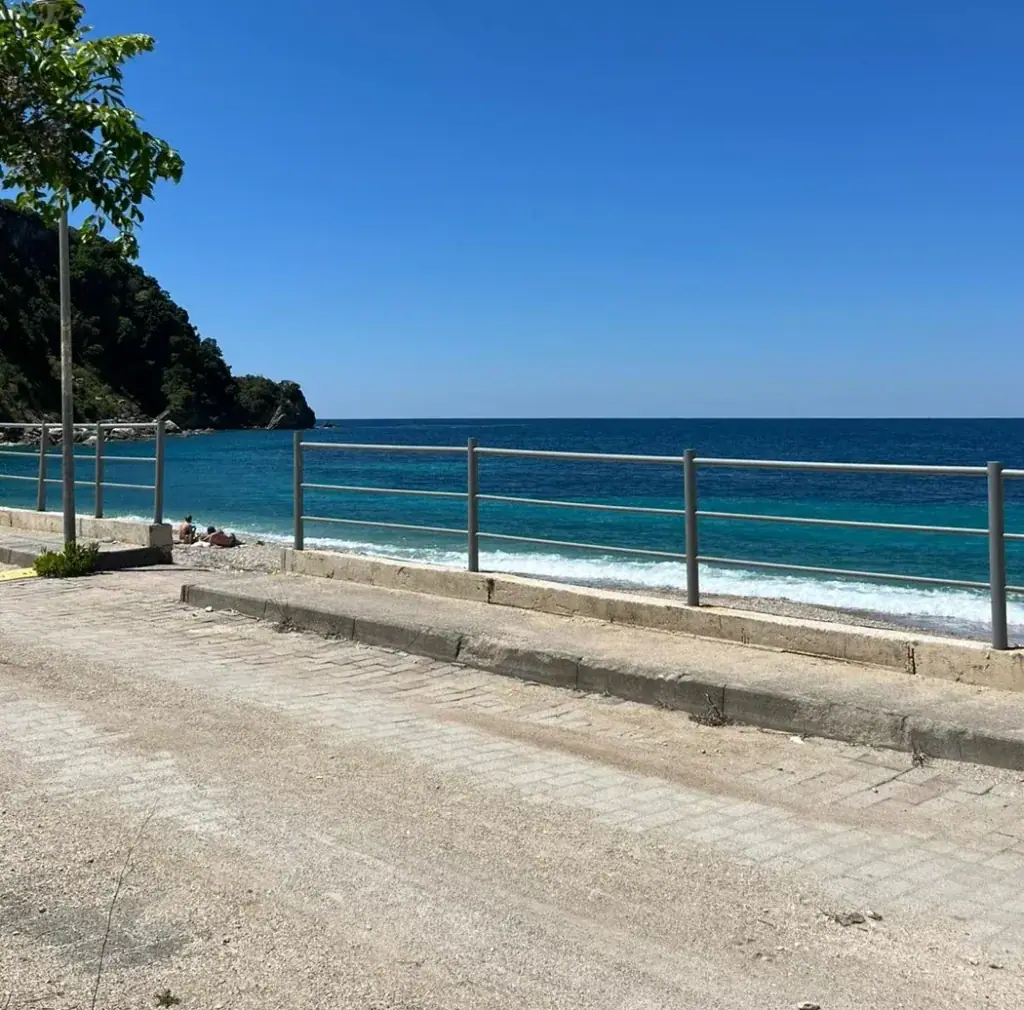 The shore road and railing at Potam with clear turquoise water breaking on the pebbles