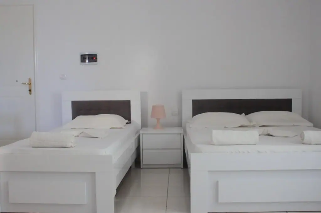 A single bed and a double bed with dark padded headboards and a small pink shaded lamp between them