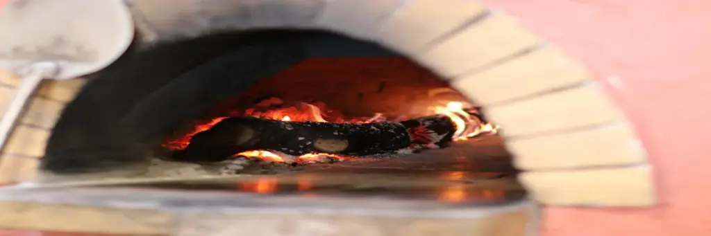 The mouth of the wood-fired oven, cream firebrick arch set in terracotta render, fire inside