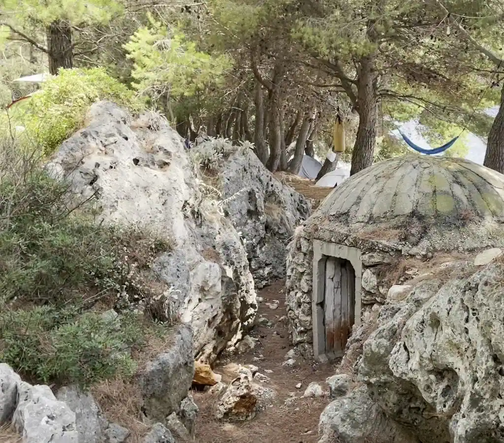 A concrete Hoxha-era dome bunker set into the limestone among pines at Pine Side Camp