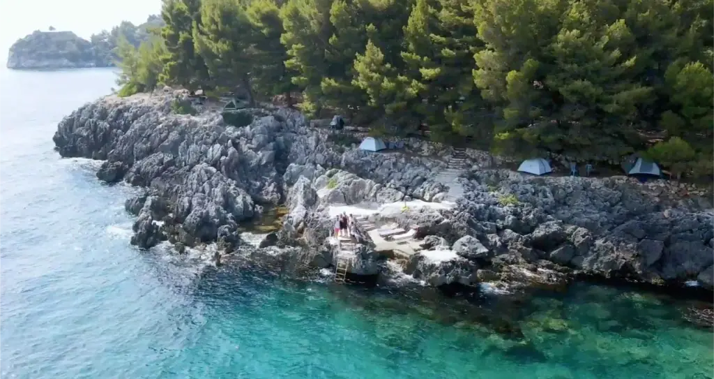 Aerial view of the pine-covered limestone headland with tents along the shore at Pine Side Camp