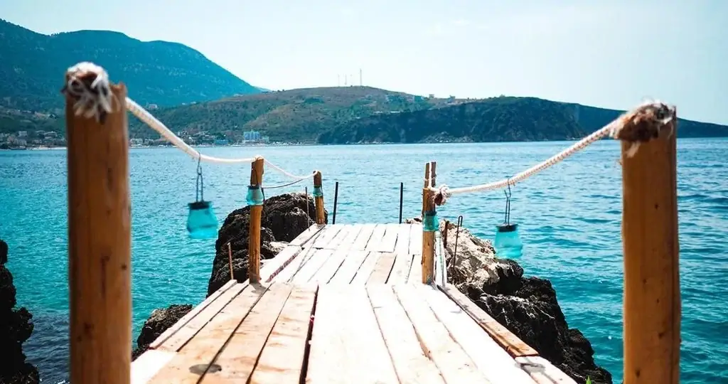 A timber jetty with rope rails and hanging lanterns running out over turquoise water