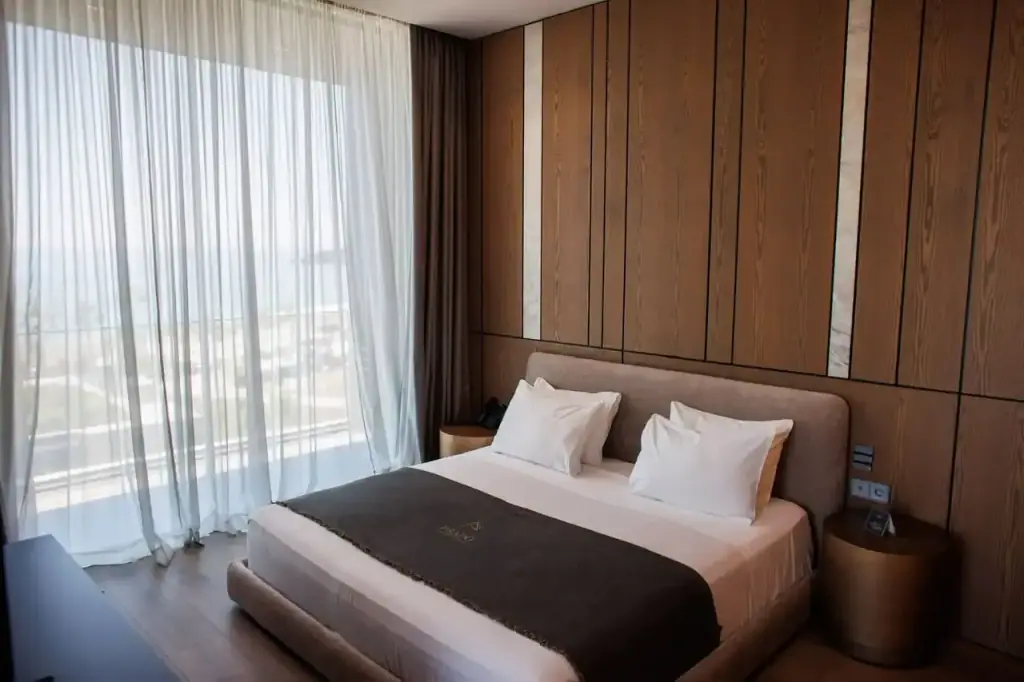 The Deluxe Suite at Prado, a wide bed against timber panelling in warm earth tones