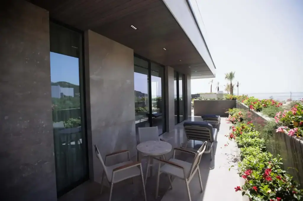 The long balcony of a sea-view Junior Suite, chairs and a table, loungers and flowering planters beyond