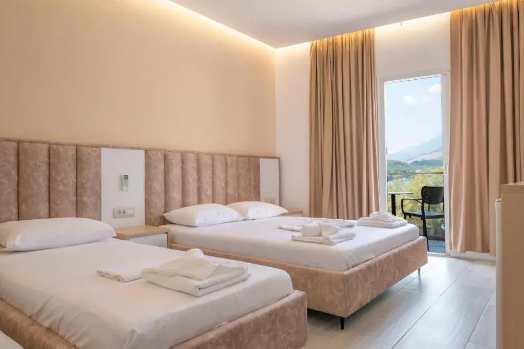 A room at Seaside Hotel with a double and a single bed against one long padded headboard, and a balcony door standing open