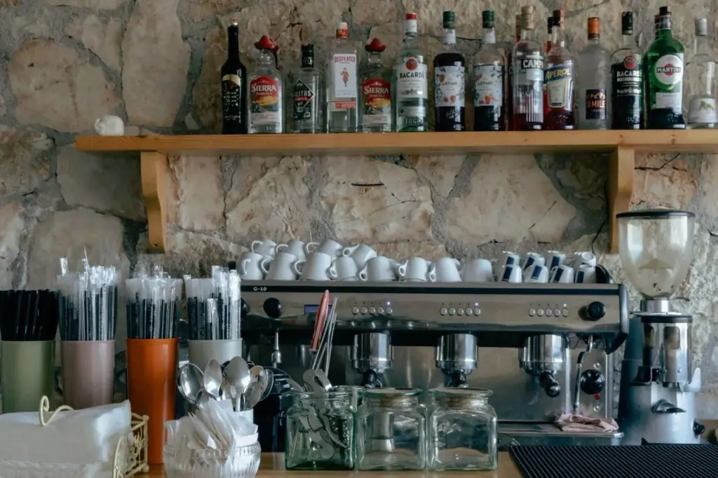 Spirit bottles on a timber shelf above glassware and an espresso machine