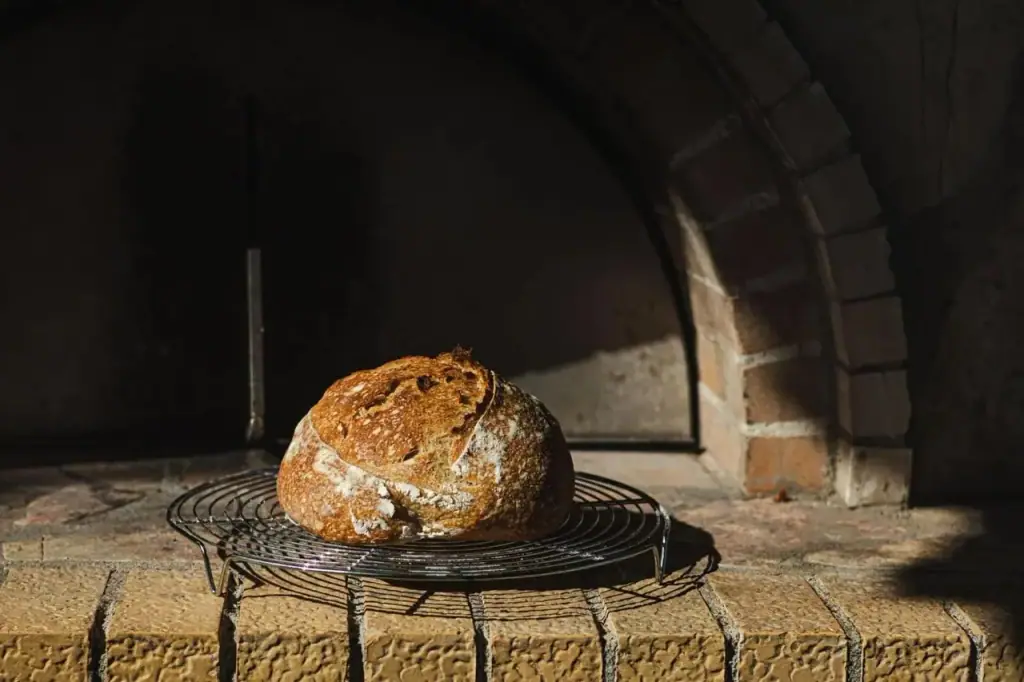 A round sourdough loaf cooling on a rack inside the mouth of the wood oven