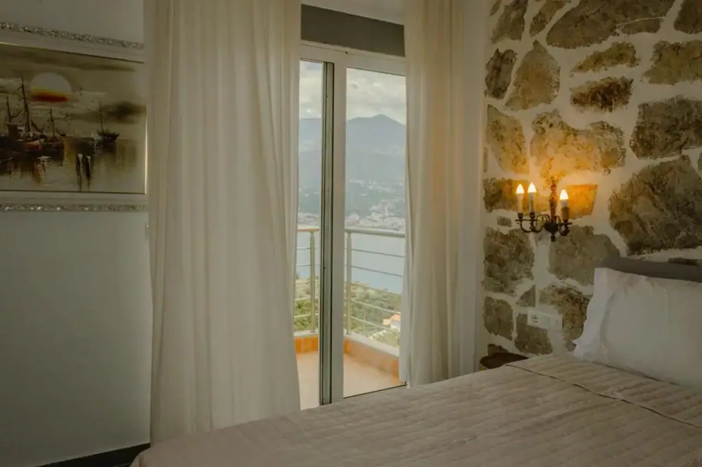 A double bed against a stone wall beside a sliding door onto a balcony over the bay